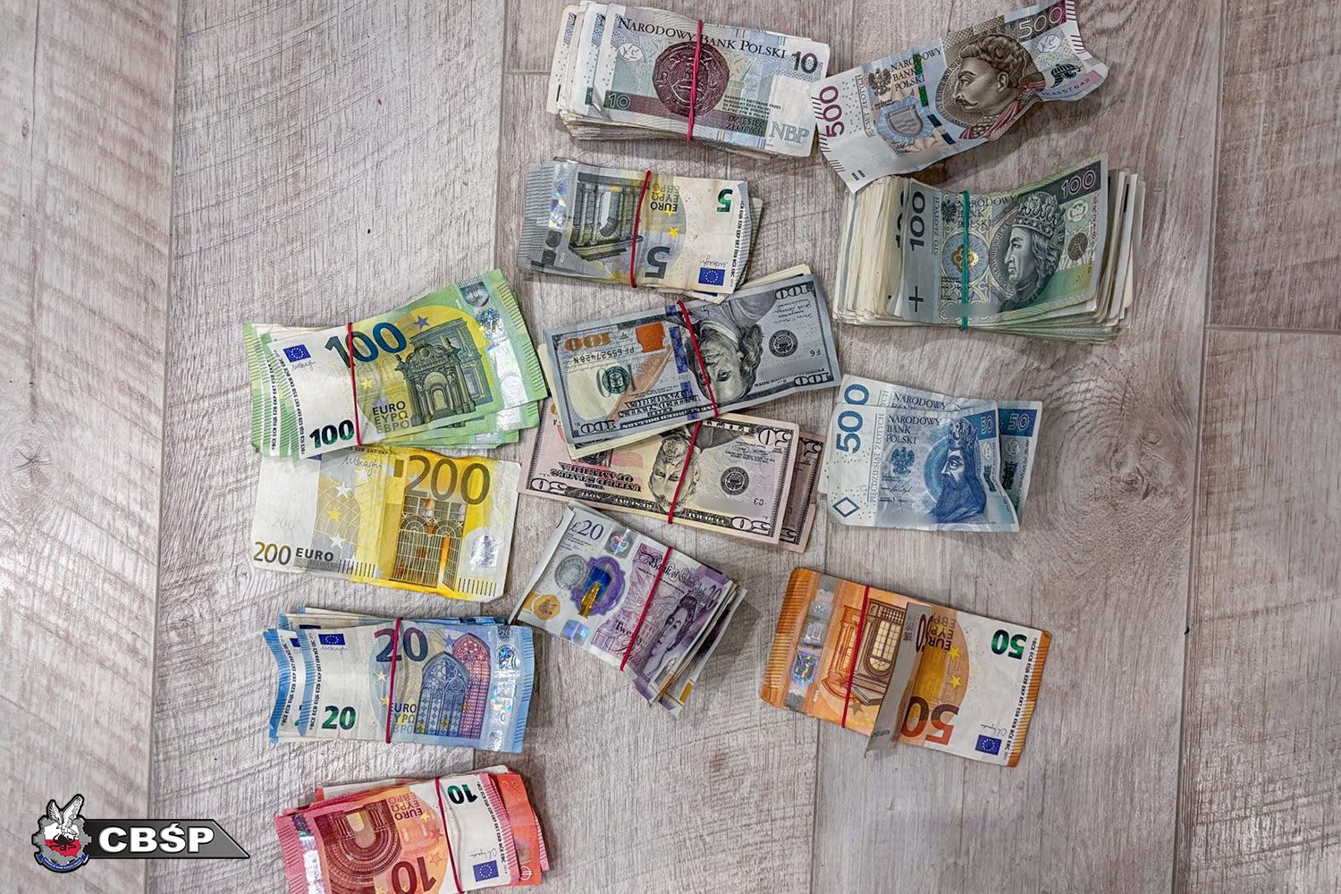 Zabezpieczona gotówka w różnych walutach – euro, dolary, funty i złotówki – rozłożona na podłodze.