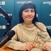 Elżbieta Puczyńska siedzi w studiu Radia AKADERA, trzyma program 40. Jesieni z Bluesem i opowiada o festiwalu. Obok mikrofon i słuchawki na stole, w tle ścianka z logo Radia AKADERA.