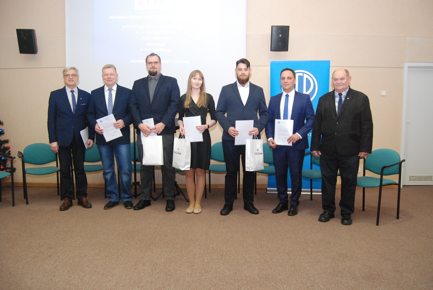 Grupowe zdjęcie laureatów konkursu SEP oraz przedstawicieli kapituły i organizatorów podczas uroczystości wręczenia nagród na Politechnice Białostockiej, uczestnicy stoją na scenie i trzymają dyplomy oraz nagrody.