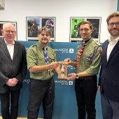 Czterech mężczyzn stoi w studiu Radia AKADERA; harcerze przekazują Adamowi Jakuciowi lampion z Betlejemskim Światłem Pokoju.