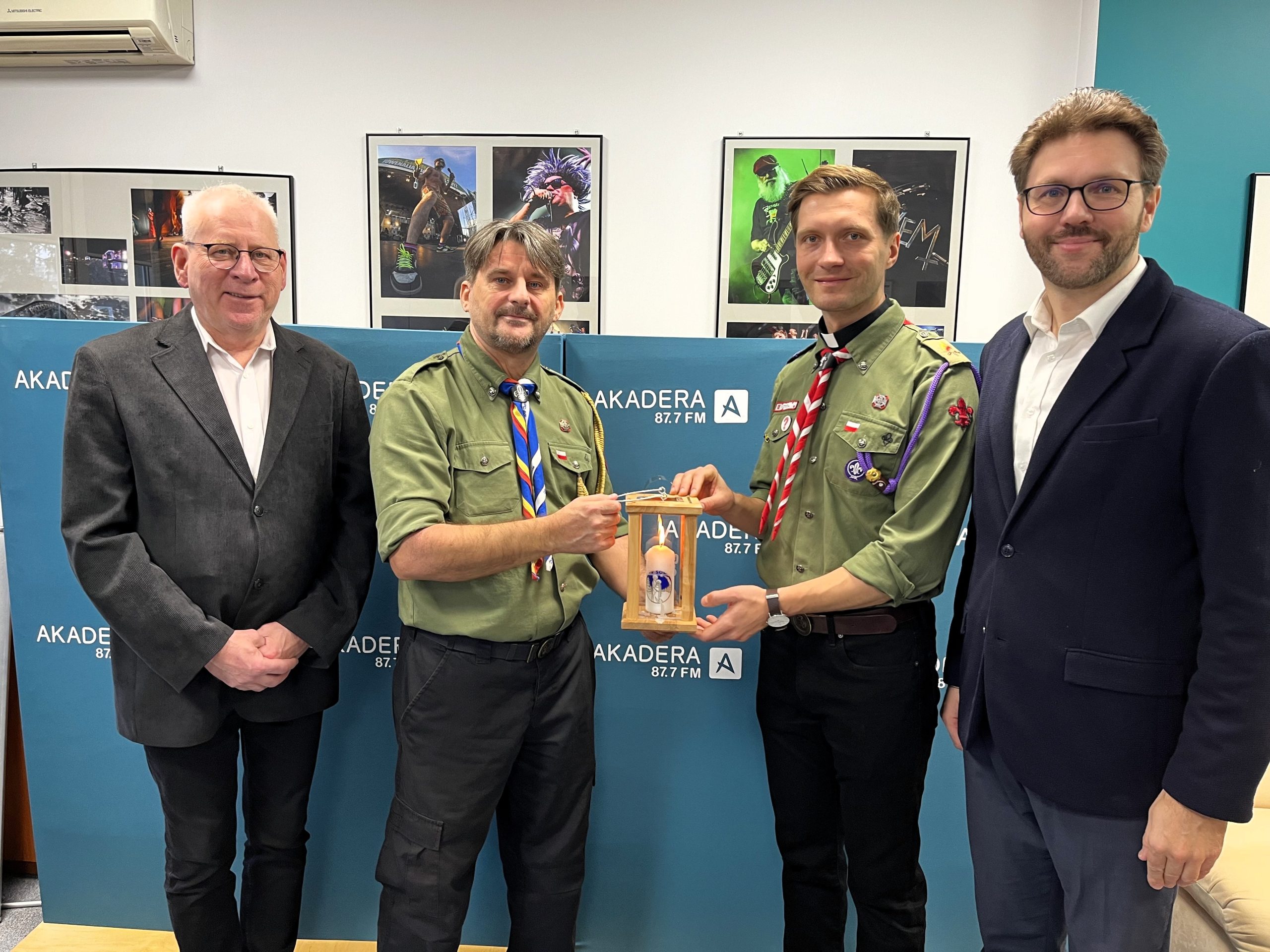 Czterech mężczyzn stoi w studiu Radia AKADERA; harcerze przekazują Adamowi Jakuciowi lampion z Betlejemskim Światłem Pokoju.
