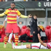 Piłkarz Jagiellonii Białystok gestykuluje z rozłożonymi rękami obok leżącego na murawie zawodnika Rayo Vallecano podczas meczu Ligi Konferencji na stadionie w Białymstoku.