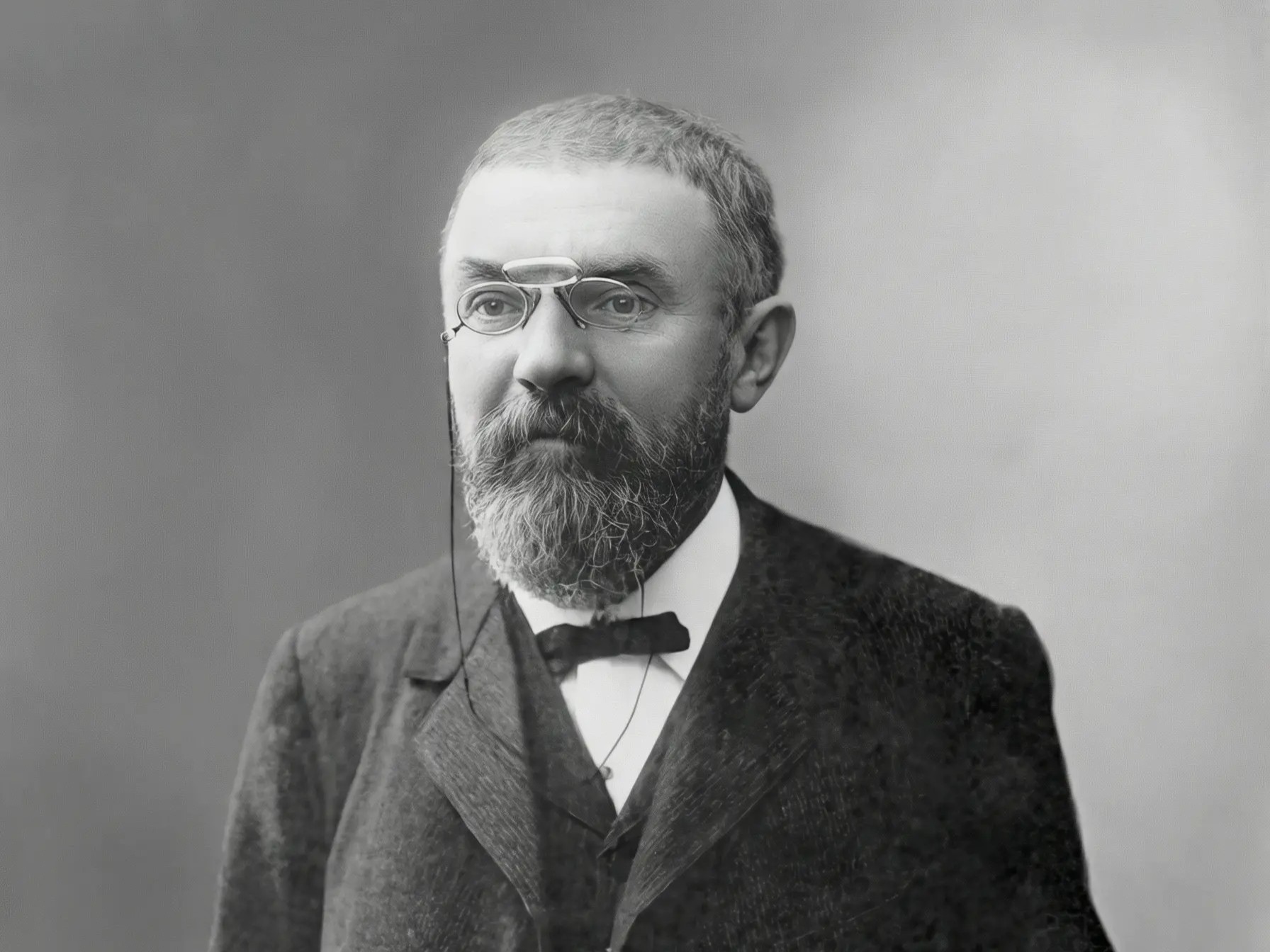 Czarno-biały portret Henriego Poincarégo w formalnym stroju, z brodą i okularami pince-nez, fotografia z 1913 roku, wykonana przed 1923 rokiem.