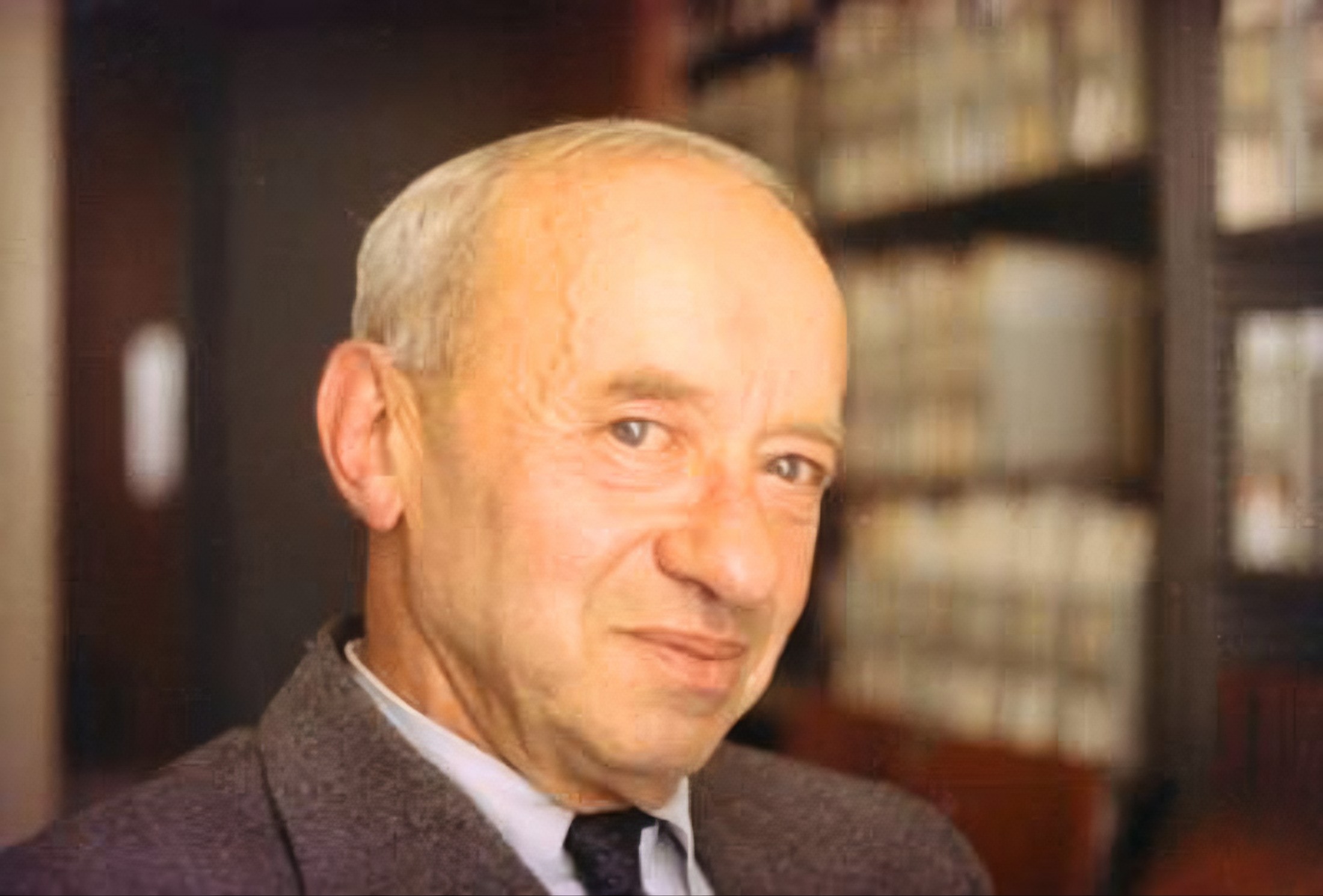 Kolorowa fotografia Alfreda Tarskiego z 1968 roku. Dojrzały mężczyzna o krótkich, siwych włosach, w marynarce i koszuli z krawatem, patrzy z lekkim uśmiechem w stronę aparatu. W tle półki z książkami.