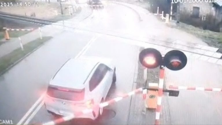 Samochód osobowy marki BMW wjeżdża na przejazd kolejowy w Hajnówce mimo włączonych sygnałów świetlnych i opuszczonych zapór, kadr z monitoringu.