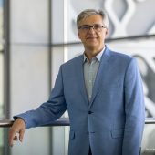 Dr hab. inż. Bogusław Butryło, prof. PB, dziekan Wydziału Elektrycznego Politechniki Białostockiej, stoi w nowoczesnym wnętrzu uczelni, opierając się o balustradę.